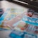 A selection of colorful lottery scratch-off tickets placed on a flat surface near a window. The image has a shallow depth of field, focusing on the tickets while blurring the background. The tickets display various games and prize amounts.