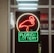 A neon sign depicting a flamingo above the words 'Florida Lottery' is prominently displayed. The sign is illuminated in bright red and green colors, and it is framed by glass panels. An 'EXIT' sign is visible in the background.